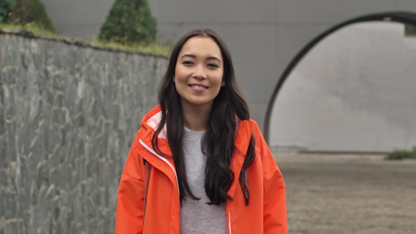 Young asian beautiful positive woman walking outdoors in orange coat.