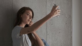Happy pretty brunette woman making selfie on smartphone while posing near the wall at home