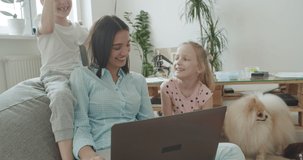 Happy mom and cute kids having fun talking using laptop at home, smiling mother teach little children online shopping. Young woman works from home. Self-isolation. 4k video footage slow motion