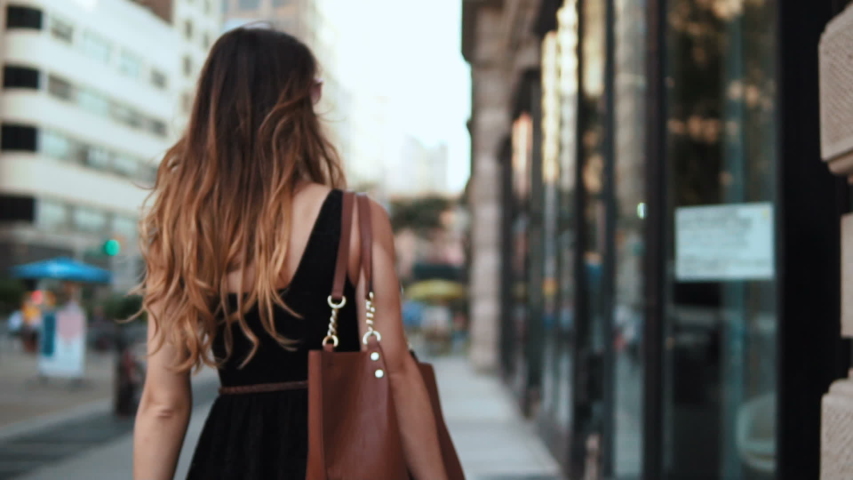 Back view of young beautiful woman with shopping bags walking through the street in downtown. Slow motion. | Shutterstock HD Video #1050650407