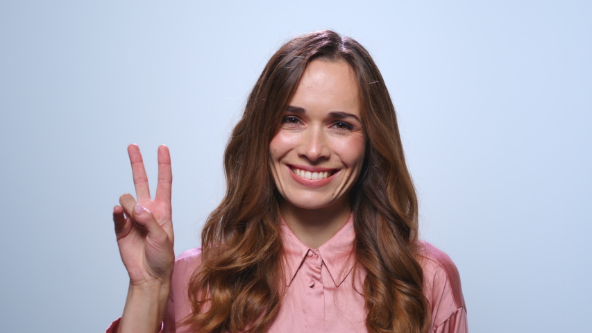 Young businesswoman showing v sign in studio. Portrait of smiling business woman showing peace sign on blue background. Closeup female professional showing victory gesture. Confident woman portrait