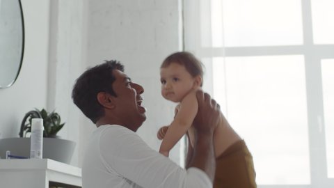 Medium shot of happy Indian father lifting adorable toddler girl and doing Eskimo kisses