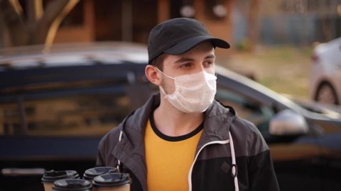 Courier in protective mask and medical gloves take order from car. Delivery boy hold pizza and coffe. Delivery service under quarantine. Coronavirus covid-19 theme