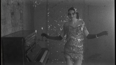 Young happy beautiful woman in bright sparkling luxury silver dress, smiles gown fluttering dances in room near piano, black and white old fashioned film with added noise. 20s stylized carnival party