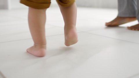 Tracking with low-section of unrecognizable toddler walking barefoot on tiled floor