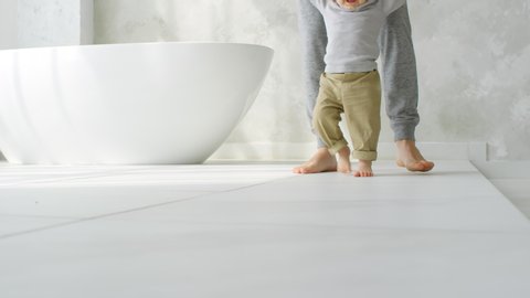 Low-section of unrecognizable father holding hands of cute baby learning to walk in bathroom