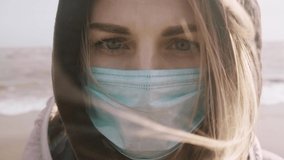 woman in a medical mask on her face against the background of a cold sea in a jacket - Powered by Shutterstock - Get 15% off with code: PIKWIZARD15