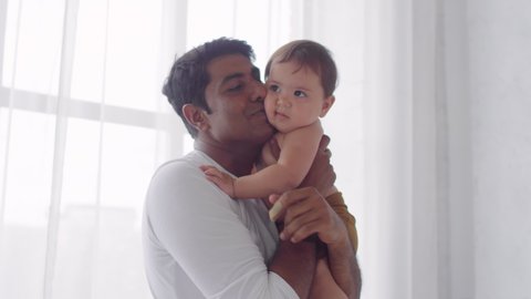 Handheld portrait shot of happy Indian father holding cute toddler girl and looking at camera: film stockowy