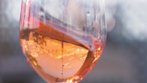 Tasting rose wine on a bar patio. Drinking pink rosé all day. The crisp, refreshing summertime wine swirls around the wineglass in slow motion.