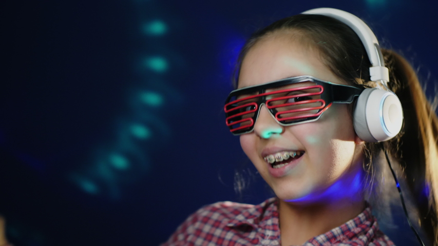 Portrait of a cheerful pretty girl with braces, wireless headphones and neon modern glasses listening to music, dancing and laughing. Closeup portrait