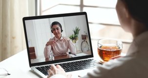 Indian female online teacher, customer service support manager wearing headset consulting client, student, remote worker in webcam video call virtual conference on laptop screen. Over shoulder view