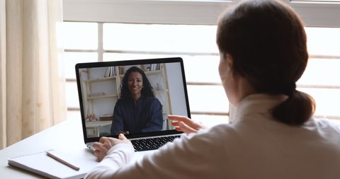 Diverse business women video calling working from home office. Over shoulder laptop screen view of female recruiter, hr manager interviewing african candidate, consulting client in webcam virtual chat