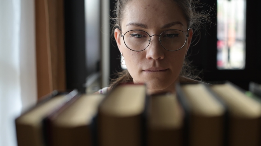 Girl student chooses a book and takes it from the shelf, close up, selective focus | Shutterstock HD Video #1050675793