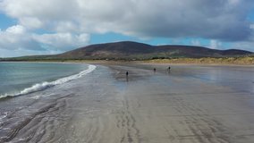 
Aerial Push in and Up of Girl and a few people walking down ventry beach in Ireland with mountains in background