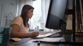 A young Spanish woman teaches video communication in isolation. Beautiful girl freelancer works from home. Businesswomen at work in front of a laptop. Home furnishings. Cozy home light.