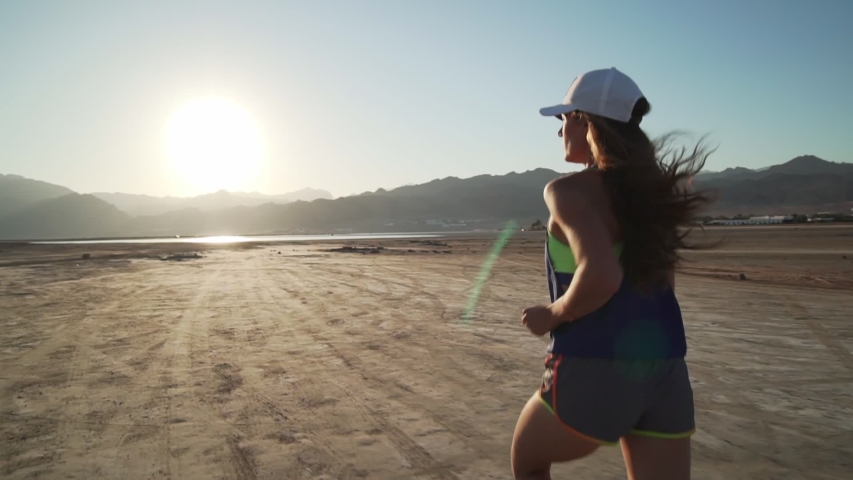 Rear view of fit young woman  jogging in dry desert at sunrise rapid slow motion