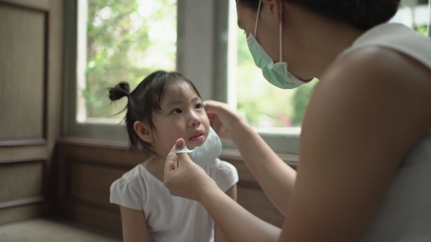 Asian mother wearing medical face mask for daughter. COVID-19, Handheld shot Royalty-Free Stock Footage #1050692755