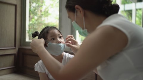 Asian mother wearing medical face mask for daughter. COVID-19, Handheld shot