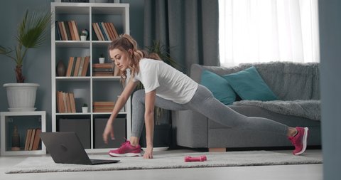 Sportswoman in activewear doing fitness exercises with help of her instructor online on laptop. Training on distance. Domestic workout and self motivation.