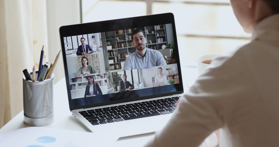 Over shoulder view of female remote worker participating group virtual chat meeting by webcam conference chat working from home office. Professional business team on laptop screen online video call. Royalty-Free Stock Footage #1050707056
