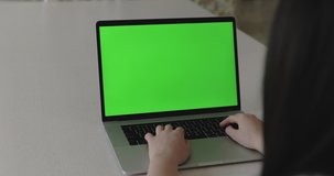 Female person typing on laptop keyboard with green screen and gestures with her hands while talking online on table. 4K