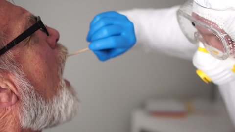 Close up portrait of a doctor in a protective suit takes a swab from the throat of an elderly senior man pensioner. Non-invasive diagnostic method by PCR reaction. Rapid test covid 19, SARS-CoV-2, IgM