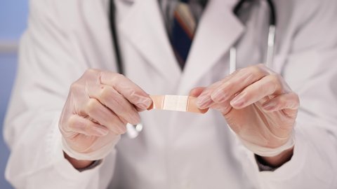 Professional medical doctor, wearing a white lab coat and a stethoscope and protective gloves , holding a adhesive band aid bandage