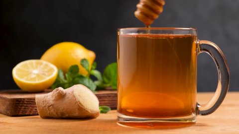 Cup of hot tea with ginger root, lemon and honey. Adding natural raw honey to cup of hot tea. Vitamin C drink, immune system boost