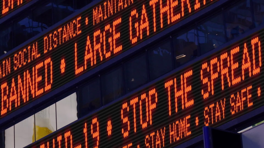 Closeup view of a Times Square ticker says stay safe and say home and large gatherings are banned. Physical distancing was a common practice to slow the spread of COVID-19 during the pandemic of 2020. Royalty-Free Stock Footage #1050713545