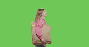 Woman with rag reusable bag with groceries food isolated on green screen background. Girl in pink hoodie walking over chroma key. 4k raw footage video side view