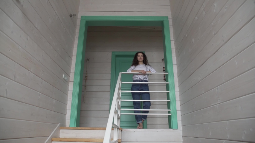 a curly-haired girl stands on the second floor near the stairs and poses for the camera in the General plan of the frame.