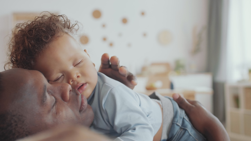 Close up of sweet African baby boy lying on his father and sleeping. Caring man patting his child on back | Shutterstock HD Video #1050714991