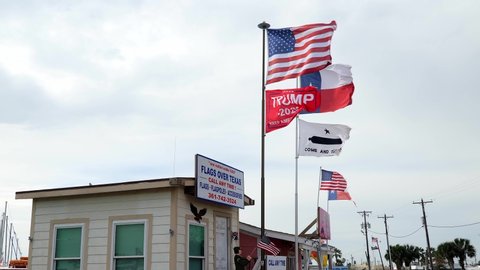 ROCKPORT, TX - 3 FEB 2020:  Flags Over Texas, a flag store with various flags, including TRUMP 2020, waving in the breeze over the shop. Hand held slow motion clip.