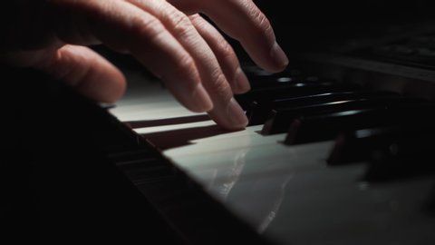 Pianist plays gentle classical music on a beautiful grand piano with one hand close-up in slow motion. Piano keys close up in dark colors. Student trains. Hands of a male in low key light. 4K