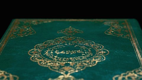Lisbon, Portugal - April 8 2020 Islamic Holy Book Koran's Cover Close Up Shot. Some Verses and Ornaments in Arabic Language. It Means 'God', 'God is Great' Book on Turning Table. 4K Resolution UHD.