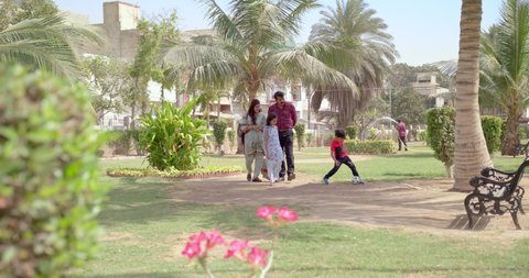 Father & mother talk while walking in the park as child plays with ball, daughter a little reluctant 