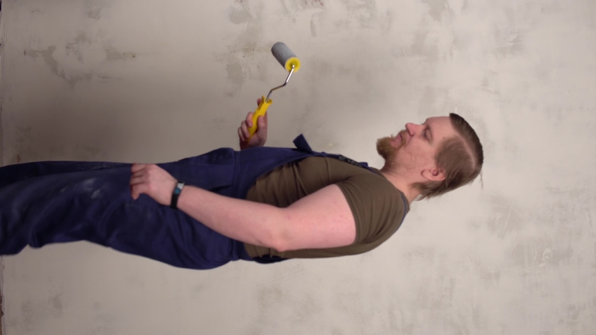 Timelapse a red-bearded, muscular male house painter with a paint roller applies gray paint to the prepared wall, the vertical orientation screen 9:16.