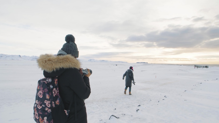 young woman photographer takes pictures of her friend at sunrise in Solheimasandur dc3 Plane Crash in Iceland