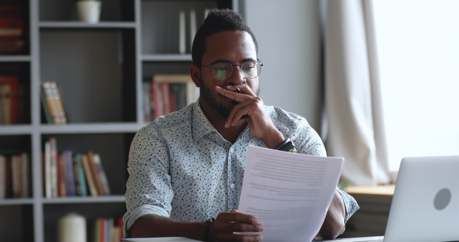 Thoughtful young african man looking through reading paper document, feeling stressed about banking loan money debt notification. Depressed biracial guy frustrated about high bills, dismissal notice. Royalty-Free Stock Footage #1050724879