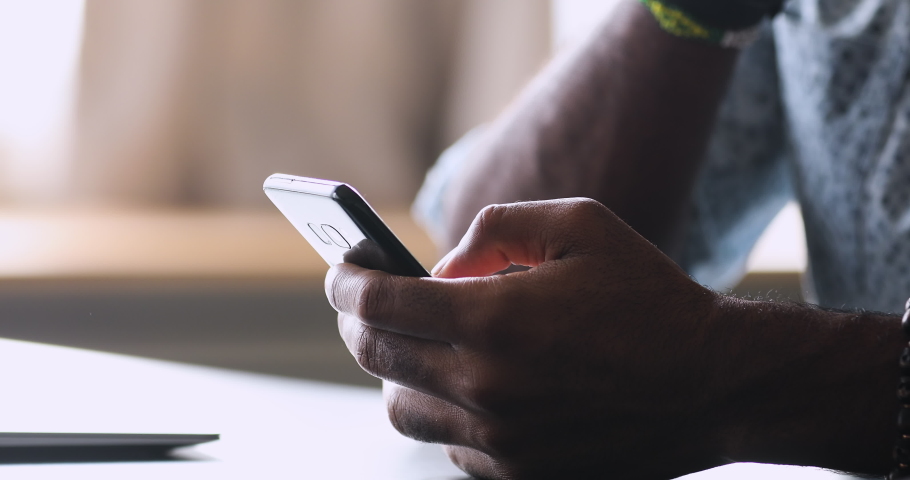 Close up young african american guy holding cellphone in hands, scrolling personal page in social network, looking at photos, reading news in media, using dating application, web surfing information. Royalty-Free Stock Footage #1050724885