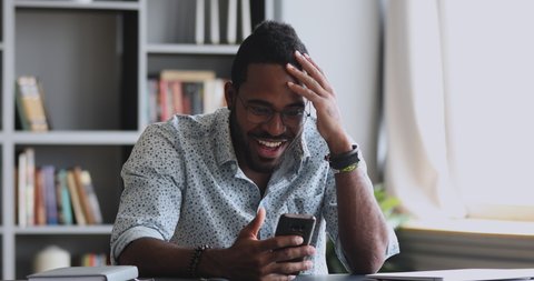 Overjoyed young african american man received message with unexpected good news, amazed by online lottery win notification. Happy millennial guy excited by bet bid, application mobile game free usage.
