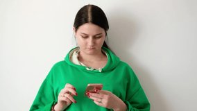 woman near a white wall looks at a smartphone, after which she looks at the camera and smiles