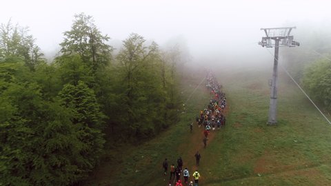 Aerial shot of large group of unrecognizable people running up a ski slope during summer on a foggy day. 