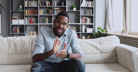 Happy young handsome african american male blogger in glasses sitting on sofa, recording video for followers in social networks. Skilled professional sharing knowledge educating on personal channel.