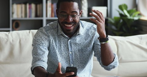 Excited young african ethnicity guy looking at mobile phone screen, reading message with unbelievable news. Happy millennial biracial hipster man feeling overjoyed about lottery win notification.