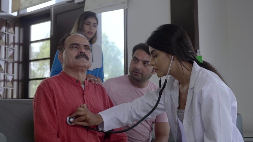 A wide shot of a doctor interacting with concerned family members about health of an old patient. A friendly female physician talking checking examining grandfather senior elder man in the house | Shutterstock HD Video #1050741001