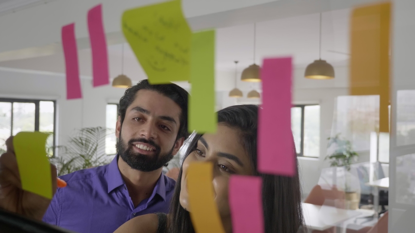 A smiling happy office corporate woman female girl using sticky notes for brainstorming session with male man colleague employee worker. A businesswoman leader planning with business partner. Royalty-Free Stock Footage #1050741019