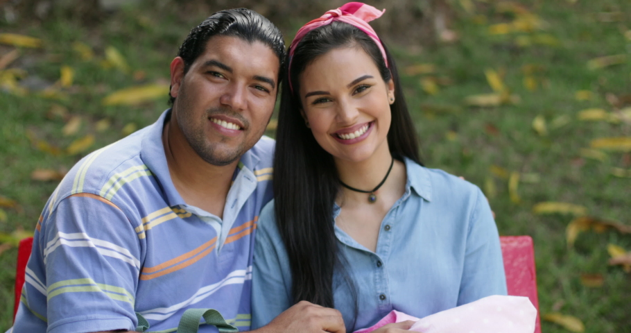 Slow Motion Portrait of Young Hispanic Smiling Couple With Their Newborn Baby Infant Sitting Outdoors On a Bench of a Public Park During a Sunny Day Looking at Camera 4k | Shutterstock HD Video #1050744709