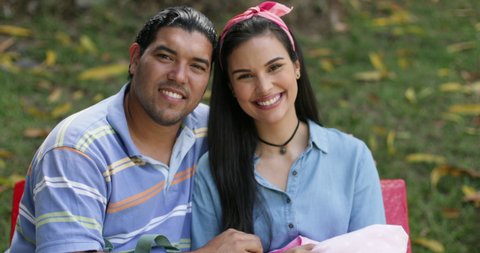 Slow Motion Portrait of Young Hispanic Smiling Couple With Their Newborn Baby Infant Sitting Outdoors On a Bench of a Public Park During a Sunny Day Looking at Camera 4k
