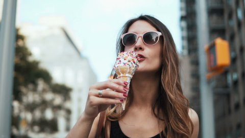 Portrait of young beautiful woman walking in downtown in sunglasses and eating the ice cream. Slow motion.